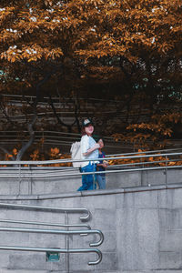 Young man sitting on railing against trees