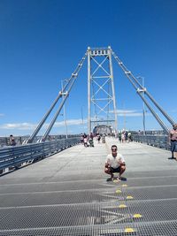 Man crouching on bridge against clear blue sky