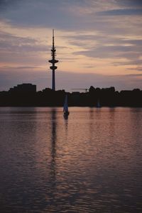 Silhouette tower by lake against sky during sunset