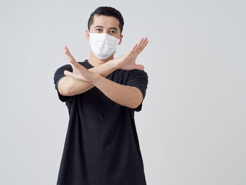 Portrait of man wearing mask gesturing while standing against white background