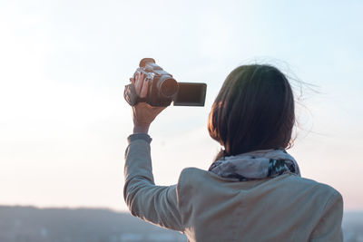 Rear view of woman photographing against sky