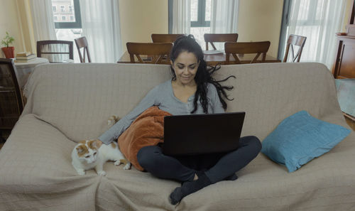 Young woman using smart phone while sitting on sofa