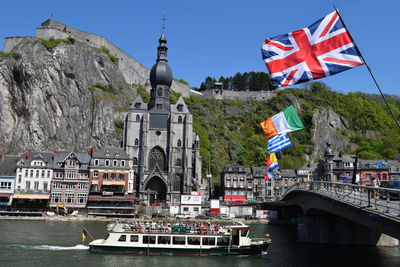 Ferry sailing in river by notre dame de dinant against sky