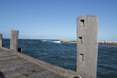 Wooden post by sea against blue sky