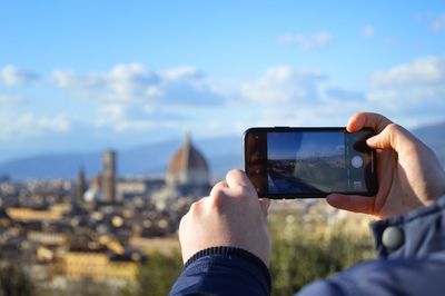 Midsection of man photographing cityscape against sky