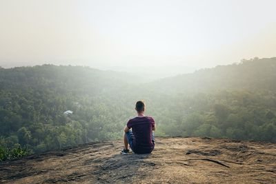 Rear view of man sitting on mountain against sky