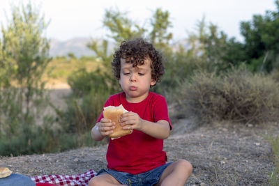 Funny picnic situation of a boy eating a sandwich in the mountains with enthusiasm sitting