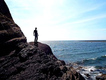 Man standing on rock by sea against sky