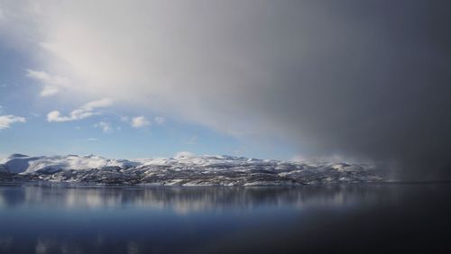 Scenic view of lake by snowcapped mountain against cloudy sky