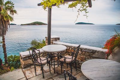 Empty chairs and tables by sea against sky