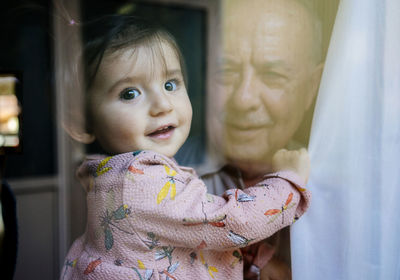 Portrait of cute granddaughter carried by grandfather seen through window
