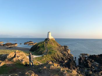 Lighthouse on rocks by sea against clear sky