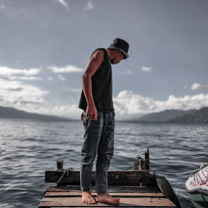 Man standing on wooden raft over sea against sky