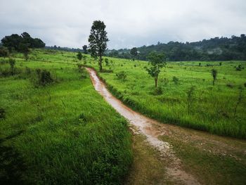 Dirt road amidst field against sky