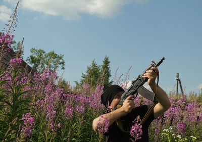 Woman holding purple flowering plants on field against sky