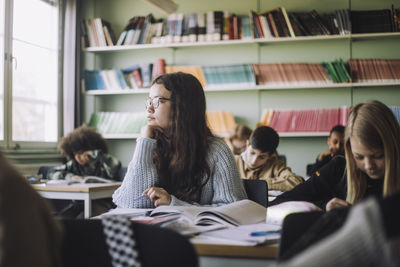 Girl with hand on chin sitting at desk during exam in classroom