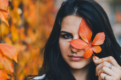 Close-up portrait of young woman with orange leaves during autumn