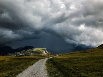 Scenic view of road amidst field against storm clouds