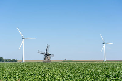 An old traditional windmill among a number of modern wind turbines under a clear blue sky