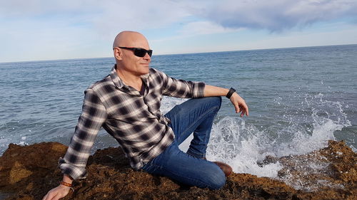 Full length of man sitting on beach against sky