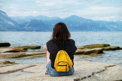 Rear view of woman sitting on rock by lake