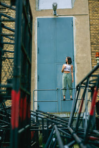 Full length of young woman standing on railing against metallic doors