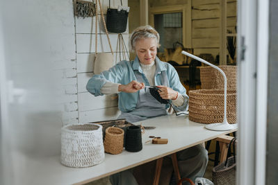 Mature craftswoman crocheting at workbench in workshop