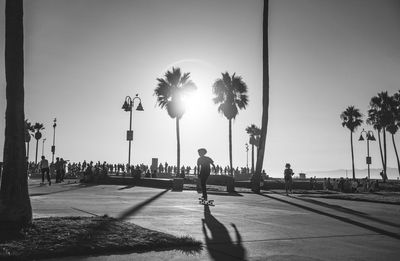 People walking on street by palm trees against sky