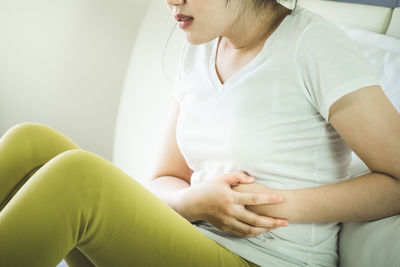 Midsection of woman with stomachache sitting on bed at home