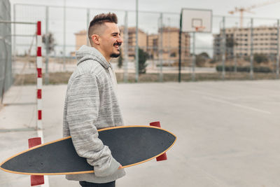 Portrait of young man standing outdoors with skateboard in hand