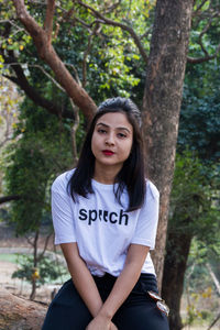 Portrait of young woman against tree trunk in forest