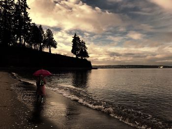Woman standing on wet shore against sky during sunset