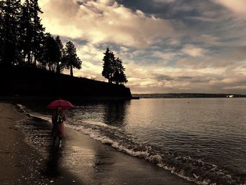 Woman walking at shore against sky during sunset