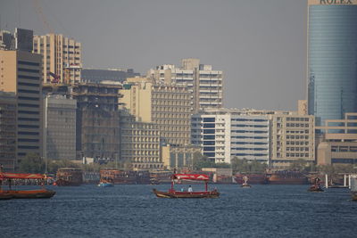 Sailboats in sea by buildings against clear sky