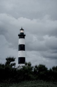 Lighthouse on field against cloudy sky