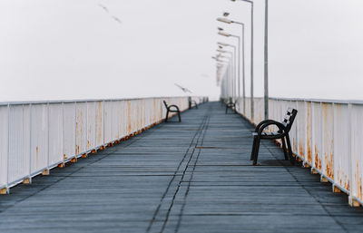 Surface level of footbridge with lamps and benches against clear sky at sea