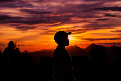 Silhouette woman standing against orange sky during sunset