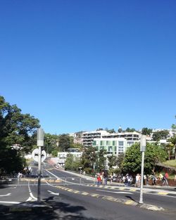 Road by buildings against clear blue sky