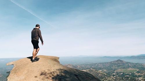 Rear view of man standing on mountain against sky