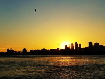 Silhouette buildings in front of river at sunset