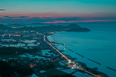 Aerial view of illuminated cityscape by sea against sky at night
