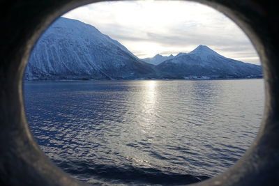 Scenic view of sea and snowcapped mountains against sky seen through window