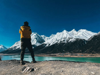 Rear view of person standing on snowcapped mountain against clear blue sky