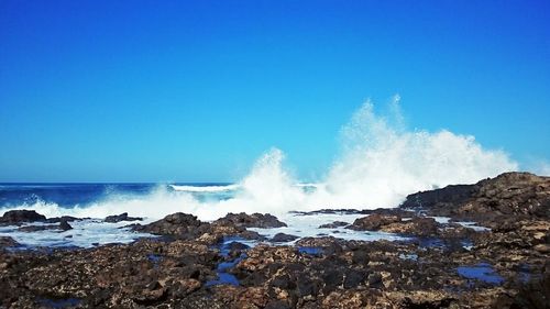 Waves splashing on rocks against clear blue sky