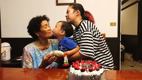 Grandson kissing grandmother by birthday cake on table at home