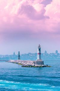 Lighthouse amidst buildings by sea against sky