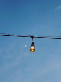 Low angle view of illuminated light bulbs against blue sky