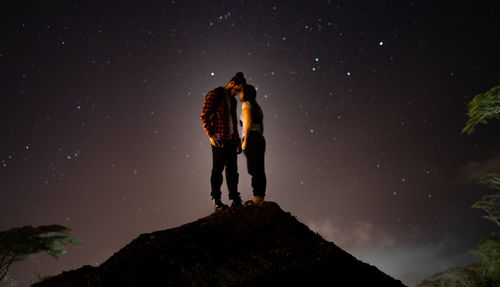 Couple standing on rock against sky at night