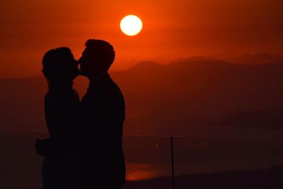 Silhouette couple embracing against orange sky