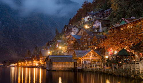 Illuminated buildings by lake against sky at night